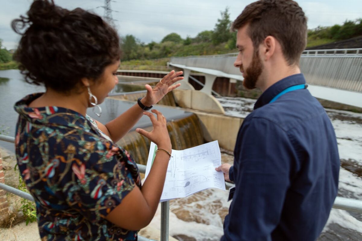Two engineers discussing plans by a water project site. Collaborative teamwork on hydropower.